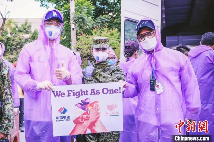 　捐赠现场，以紫色雨衣作为防护衣的志愿者，将一袋袋大米捐赠给菲律宾基层社区。宣传版上是紧握的两只手，绘以中菲两国国旗，口号是“WE FIGHT AS ONE!” 爱+慈善基金会供图 摄
