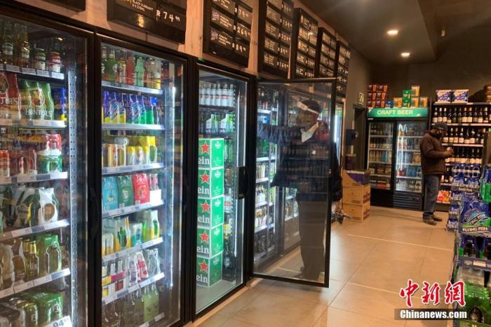 资料图：南非约翰内斯堡，一家酒类商店的店员佩戴面罩整理冰箱内的货物。 中新社记者 王曦 摄