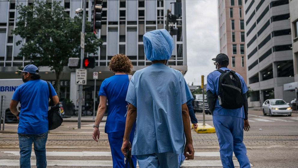 PHOTO: Medical workers and pedestrians cross an intersection outside of the Houston Methodist Hospital on June 09, 2021, in Houston.