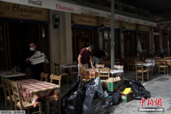 资料图：希腊雅典，一家餐馆的服务生在收拾餐桌。